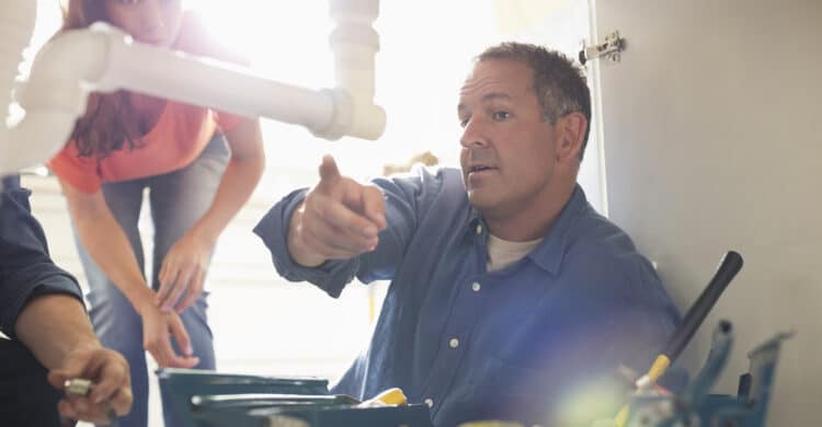 plumber looking under wink with customer