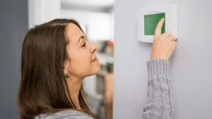 woman adjusting the heating on a home thermostat