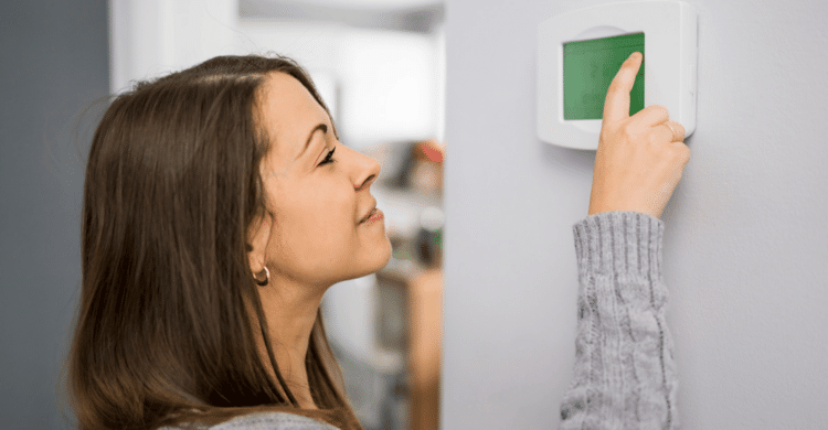 woman adjusting thermostat in home during the winter